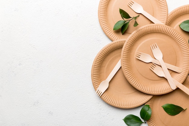 Ensemble d'assiettes, de tasses, d'ustensiles écologiques jetables réutilisables vides sur fond de table de couleur blanc clair. vue de dessus. Plats artisanaux biodégradables. Notion de recyclage. Fermer