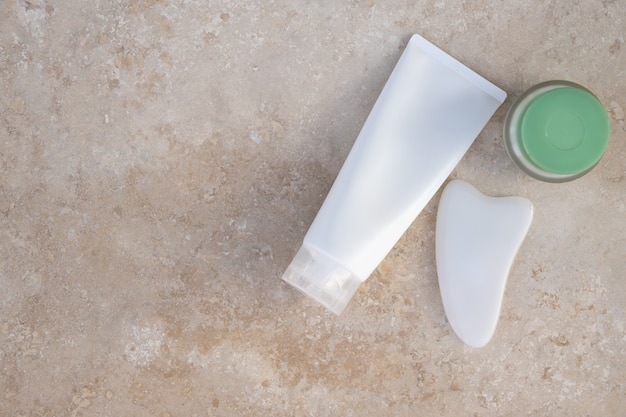 Ensemble de beauté. Masseur grattoir gua sha blanc, gel moussant, crème sur une surface texturée légère. Espace de copie, mise à plat. Concept beauté, soins personnels, soins corps visage, spa à domicile, bien-être, préservation de la jeunesse.