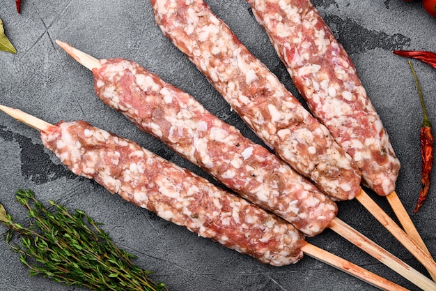 Ensemble de brochettes de mouton d'agneau hachées et en forme, avec des ingrédients de gril, sur fond de table en pierre grise, vue de dessus à plat