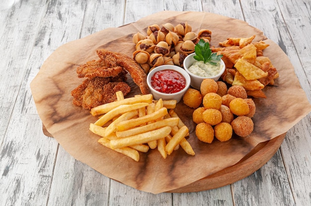 Un ensemble de collations pour la bière. Nuggets, frites, boulettes, onion rings et frites. Avec sauce tomate et fromage. Sur une planche en bois ronde. Fond en bois clair. Vue d'en-haut.