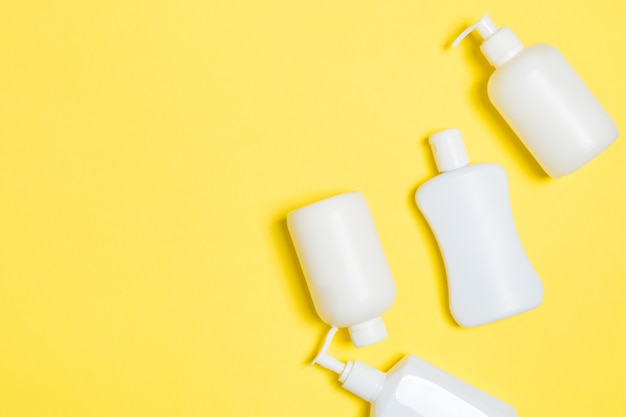 Ensemble de contenants cosmétiques blancs isolé sur fond jaune, vue de dessus avec espace copie. Groupe de contenants de bouteilles de soins corporels en plastique