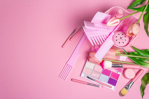 Ensemble cosmétique de maquillage et peignes à cheveux sur rose.