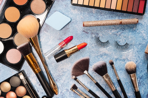 Ensemble de cosmétiques décoratifs, pinceaux de maquillage sur fond bleu. la vue d'en haut