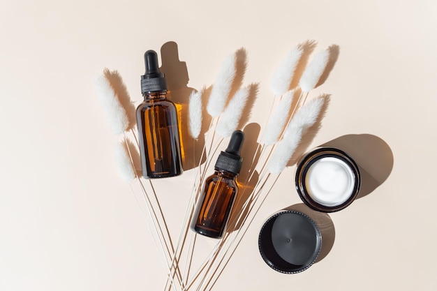 Ensemble de cosmétiques naturels écologiques sur fond beige Flacon compte-gouttes en verre ambré avec huile essentielle et pot de fleurs séchées hydratantes Vue d'en haut