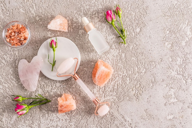 Un ensemble de cosmétiques et un rouleau de quartz rose pour les soins à domicile Spa et concept de relaxation Fond de ciment gris Vue de dessus