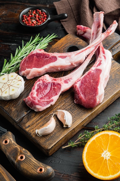 Ensemble de côtelettes d'agneau gras cru français, avec des ingrédients orange carotte, herbes, sur une vieille table en bois foncé