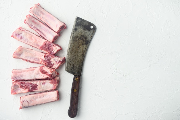 Ensemble de côtes de porc, et vieux couteau couperet de boucher, sur table en pierre blanche, vue de dessus à plat