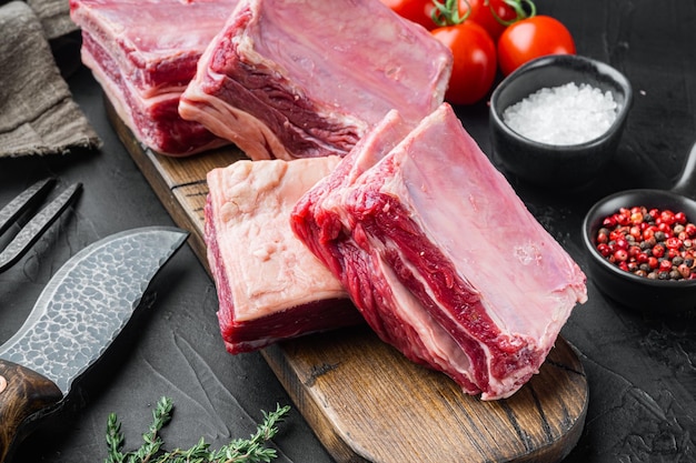 Ensemble de côtes de viande crue, avec des ingrédients, sur fond noir en pierre