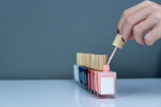 Ensemble de couleurs de vernis à ongles dans une rangée avec une main de femme tenant un pinceau d'un vernis à ongles ouvert