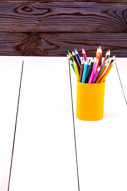 Ensemble de crayons en bois colorés en verre en plastique jaune sur une table blanche devant un mur en bois