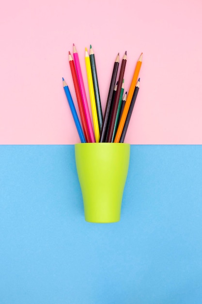 Ensemble de crayons de couleur dans une tasse verte sur une vue de dessus de fond coloré