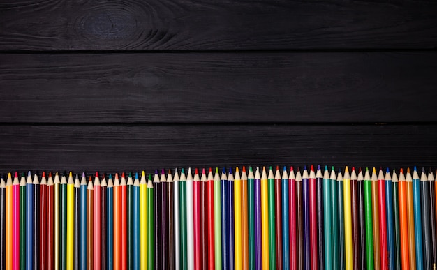 Un ensemble de crayons de couleur sur une table en bois noire. Fournitures d'impression