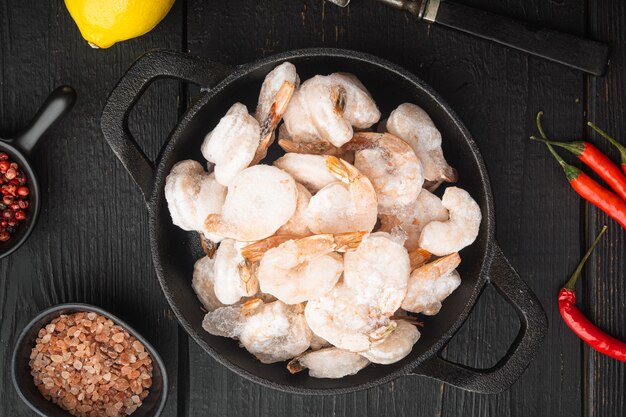 Ensemble de crevettes bouillies pelées congelées, dans une poêle en fonte ou un pot, sur une table en bois noir, vue de dessus à plat