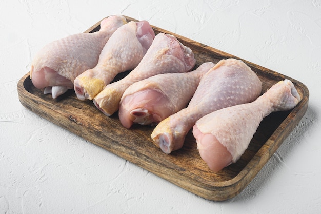 Ensemble de cuisses de poulet bio cru, sur plateau en bois, sur table en pierre blanche