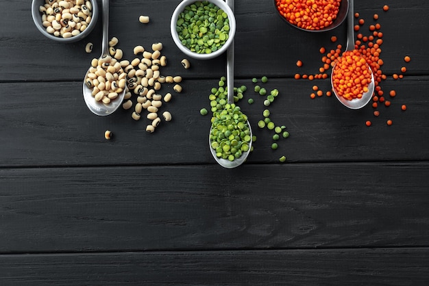 Un ensemble de différentes céréales grains anciens aliments pois verts haricots secs yeux noirs sur des cuillères sur dark wo