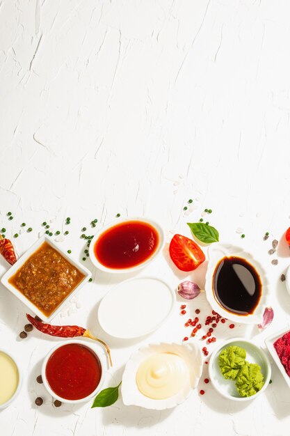 Ensemble de différentes sauces - ketchup, mayonnaise, barbecue, soja, chutney, wasabi, adjika, raifort, aïoli, marinara. Lumière dure à la mode, ombre sombre. Fond de mastic blanc, vue de dessus