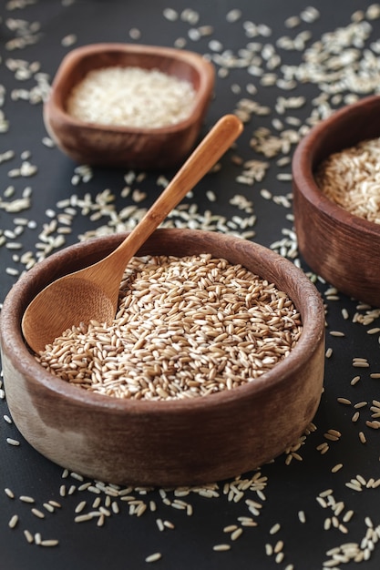 Ensemble de différents types de riz et de céréales dans les bols en bois et une cuillère en bambou