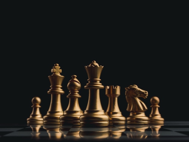 L'ensemble d'éléments d'échecs dorés, roi, tour de reine, évêque, chevalier, pion debout sur un échiquier sur fond sombre. Concept de leadership, de travail d'équipe, de partenariat, de planification et de stratégie commerciale.