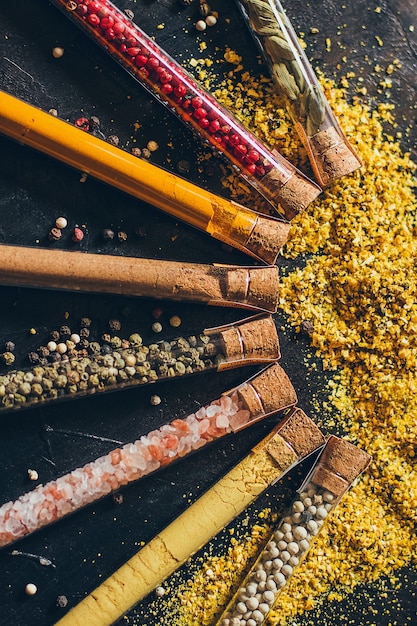 Un Ensemble D'épices Dans De Petits Pots Avec Des Couvercles En Liège. Sel Rose, Gingembre, Curcuma, Masala, Paprika, Paprika Fumé. épices Sur Une Surface Noire.