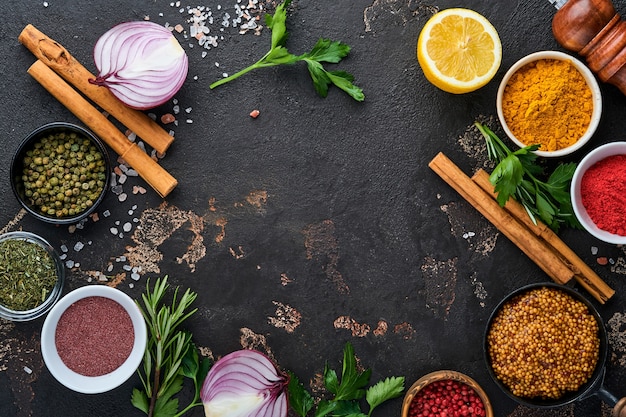 Ensemble D'épices Et D'herbes Parfumées Indiennes Sur Fond Noir En Pierre. Curcuma, Aneth, Paprika, Cannelle, Safran, Basilic Et Romarin Dans Une Cuillère. Vue De Dessus. Maquette.