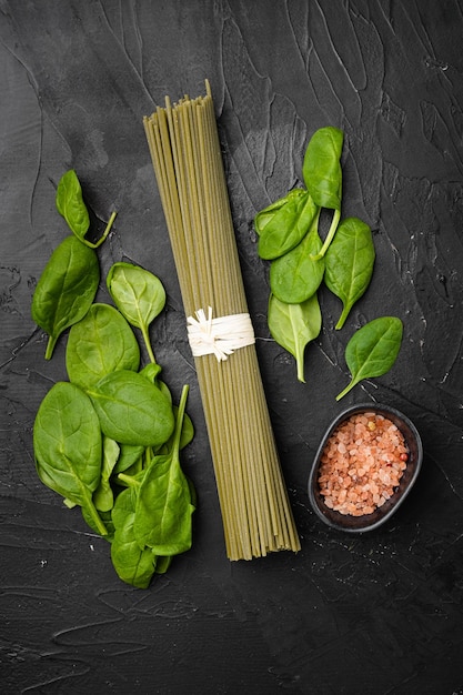 Ensemble d'épinards secs crus de spaghetti de couleur verte, sur fond de table en pierre noire noire, vue de dessus à plat