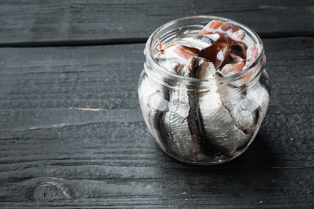 Ensemble de filets d'anchois salés, dans un bocal en verre, sur une table en bois noir