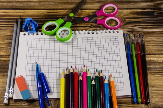 Ensemble de fournitures de papeterie scolaire. Cahier vierge, crayons de couleur, stylos, ciseaux, gomme sur un bureau en bois. Retour au concept de l'école