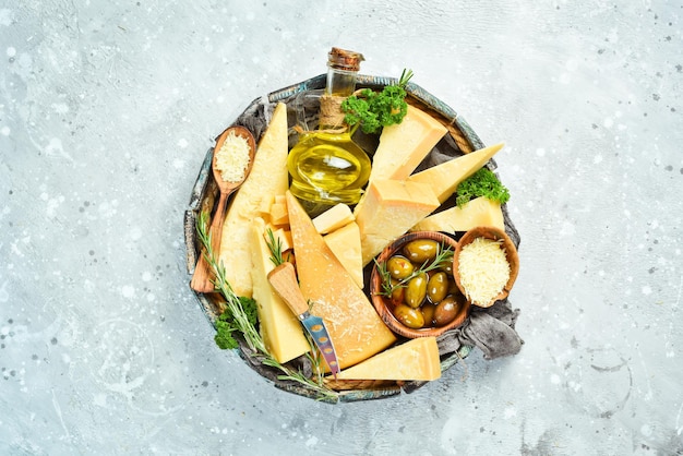 Ensemble de fromages à pâte dure dans un panier en bois. Fromage parmesan coupé en morceaux. Du fromage. Vue de dessus. Sur un fond de pierre grise.