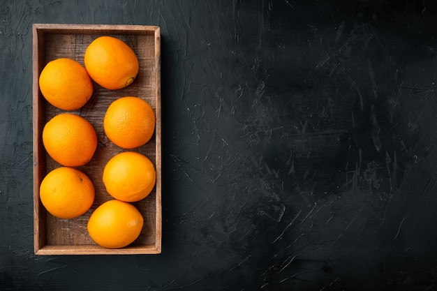 Ensemble de fruits orange mûrs, dans une boîte en bois, sur une table en pierre noire, vue de dessus à plat