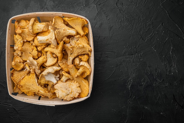 Ensemble de girolles fraîches, dans un conteneur en bois, sur fond de table en pierre noire noire, vue de dessus à plat, avec espace de copie pour le texte