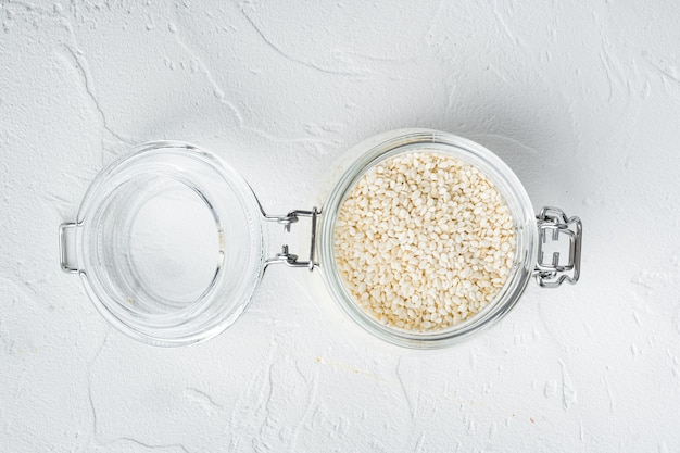 Ensemble de graines de sésame blanc, dans un bocal en verre, sur pierre blanche