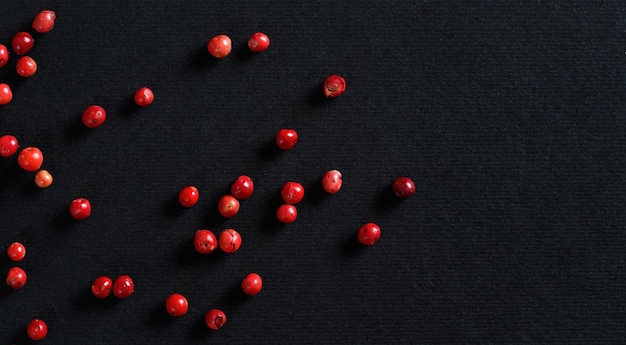 Ensemble de grains de poivre rose / rouge sur papier noir / gris, vue d'en haut, espace pour le texte à droite