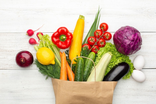 Ensemble de légumes et d'herbes dans un sac en papier sur un fond en bois blanc. Faire ses courses dans un supermarché ou un marché. Vue de dessus.