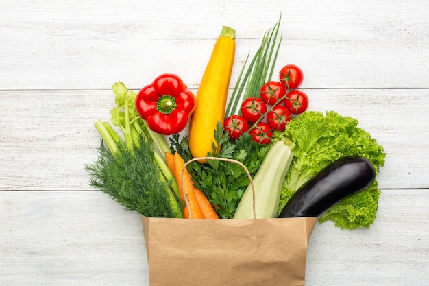 Ensemble de légumes et d'herbes dans un sac en papier sur un fond en bois blanc. Nourriture végétarienne saine.