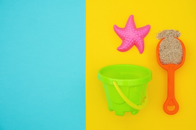Ensemble multicolore de jouets pour enfants pour jeux d'été dans un bac à sable ou sur une plage de sable fin sur fond bleu et jaune