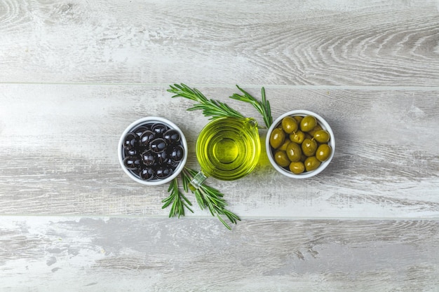 Ensemble d'olives noires et vertes sur des assiettes d'huile d'olive et de romarin sur un fond en bois gris clair vue de dessus espace de copie
