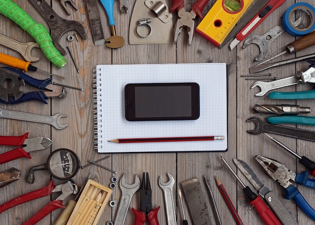 Ensemble d&#39;outils sur un plancher en bois avec un cahier et un téléphone portable au centre.