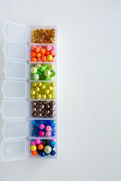 Ensemble de perles et perles de verre de différentes couleurs, formes, tailles dans un récipient sur une surface en bois blanc