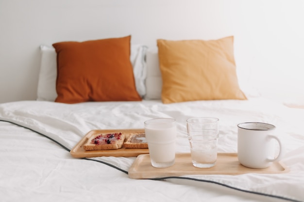 Ensemble de petit-déjeuner composé de pains et de confiture avec du lait et du café sur un lit blanc