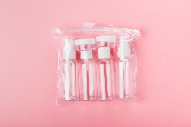 Ensemble de petite bouteille de voyage, dans une trousse de toilette transparente sur fond rose