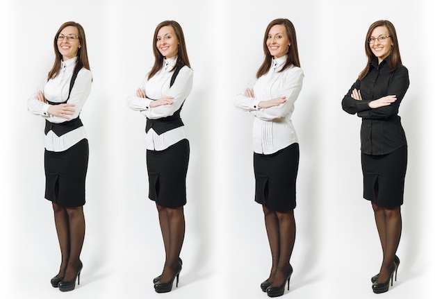 Ensemble de pleine longueur jolie jeune femme d'affaires souriante aux cheveux bruns en chemise classique noire et blanche, jupe, lunettes tenant les mains croisées isolées sur mur blanc