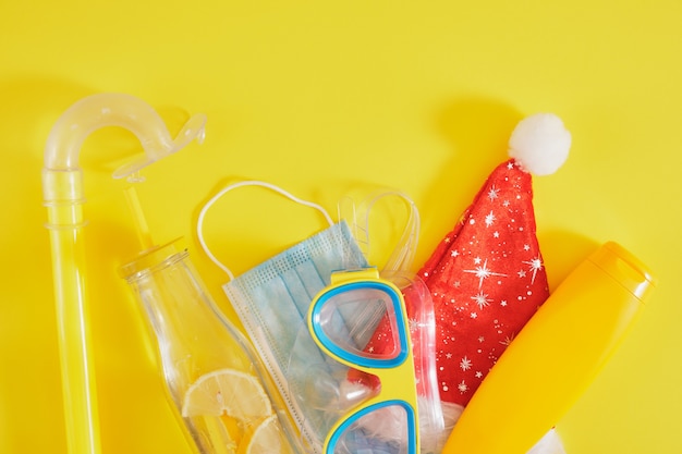 Ensemble de plongée, masque médical de protection, chapeau de père noël, crème solaire et bouteille de limonade sur fond jaune