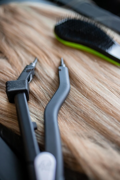 Un ensemble de plusieurs outils d'extension de cheveux pour une femme blonde dans un salon de beauté Pinces et micro tubes