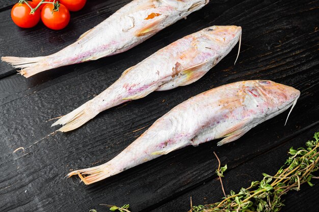 Ensemble de poisson entier frais cru de mulet ou barabulka, avec ingrédients et herbes, sur table en bois noir