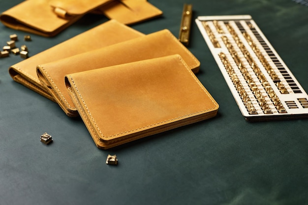 Un ensemble de portefeuilles porte-cartes de visite et porte-clés en cuir fait main jaune avec un morceau de cuir vert entouré d'outils de démonstration de produits en cuir faits à la main