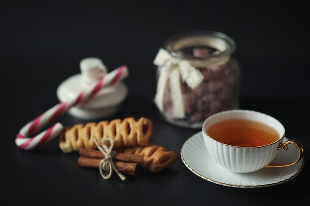 Ensemble pour le petit déjeuner. Bonbons et pâtisseries aux noix pour le thé sur fond noir. Une tasse de café et des galettes.