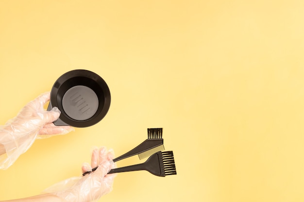 Ensemble pour la teinture des cheveux à la maison ou au salon entre les mains d'une femme avec des gants. Brosses et bol pour teinture capillaire sur fond jaune