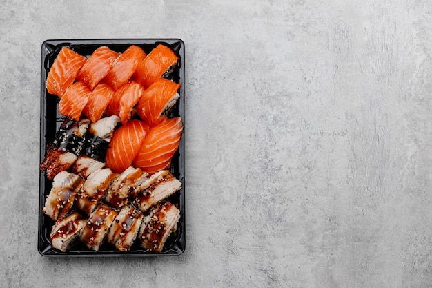 Un ensemble de quatre types de sushis dans une boîte noire sur fond gris. Vue de dessus