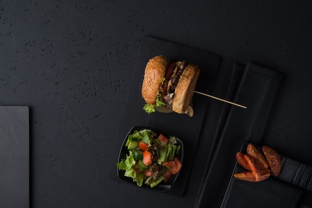 Ensemble de restauration rapide, cheeseburger avec salade et pommes de terre sur fond noir, vue de dessus