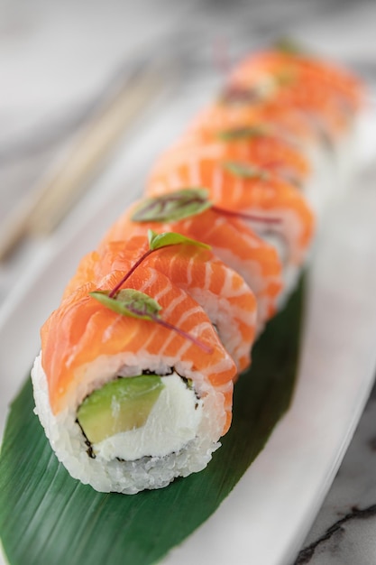 Ensemble de rouleaux philadelphie classique avec des micro-verts et des feuilles de bambou vert dans une assiette en céramique blanche avec des baguettes sur un arrière-plan en marbre texturé brillant vue latérale en gros plan